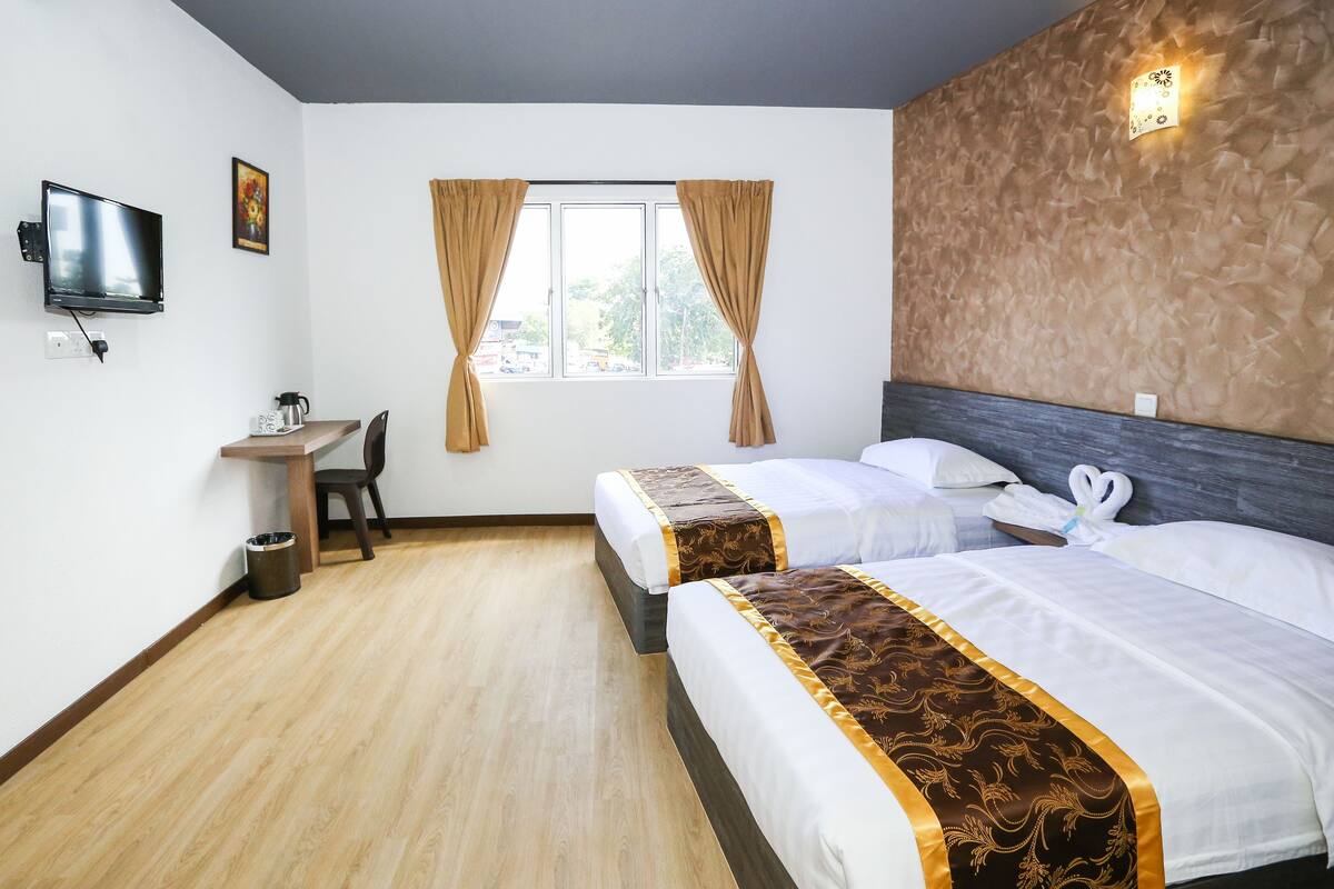 A hotel room with two beds, a desk, a chair, a TV, and a window with curtains.