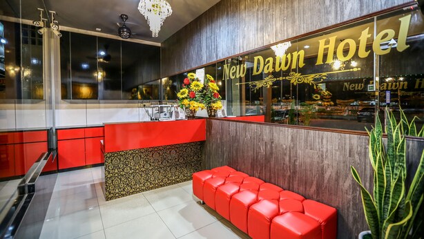 Un área de recepción con un banco rojo, un arreglo floral y un letrero que dice "New Dawn Hotel".