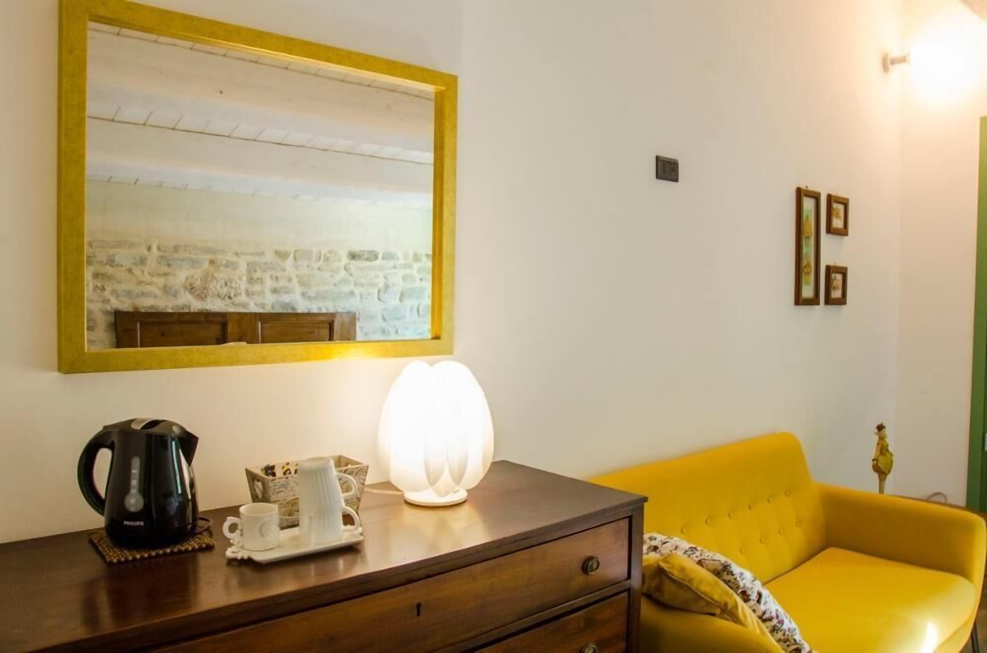 A room with a wooden dresser, a yellow sofa, a large mirror, and a wall-mounted light fixture.