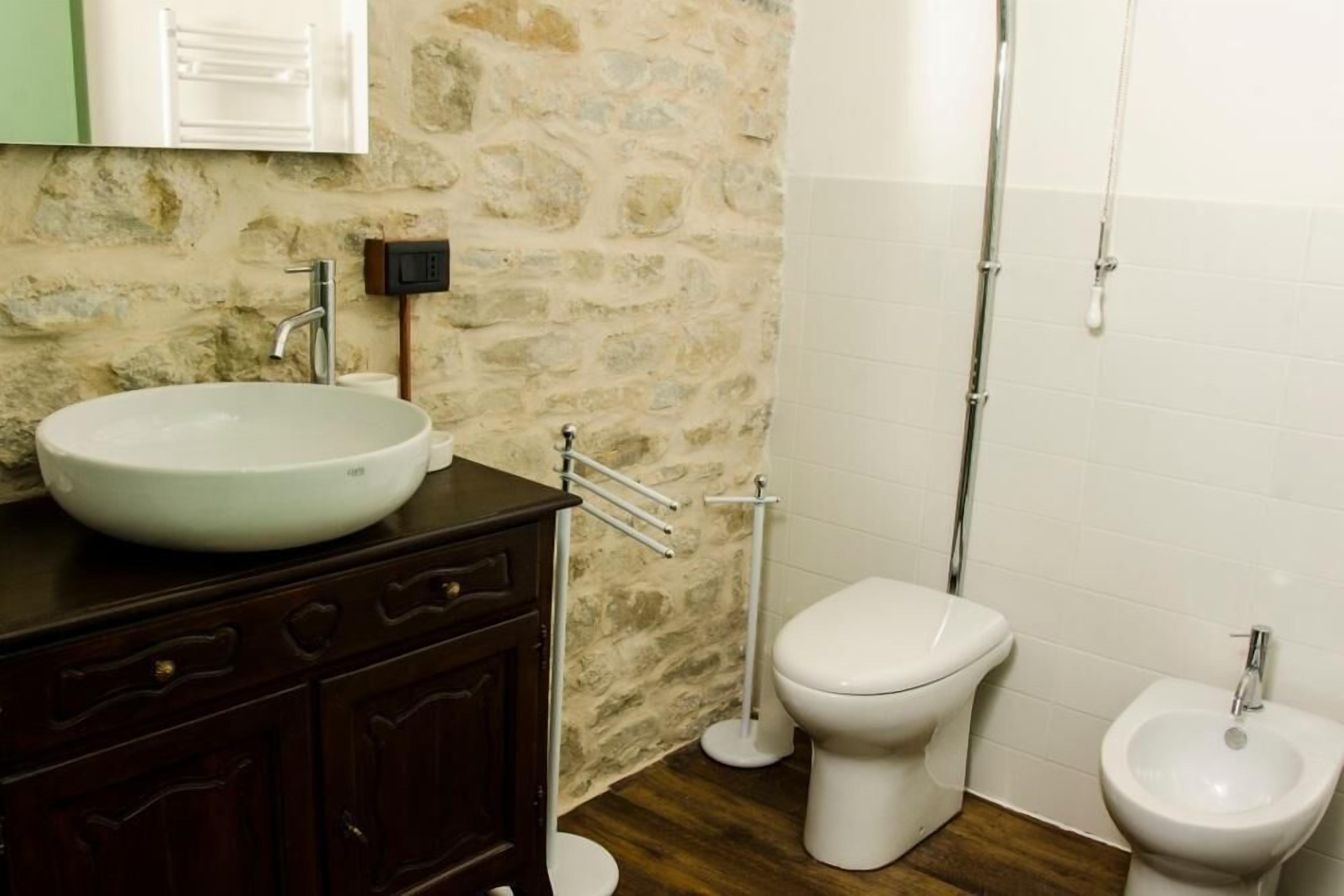 A bathroom with a stone wall, a white sink, a toilet, and a bidet.