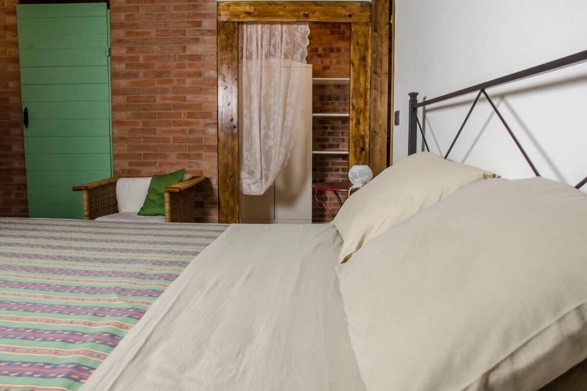Une chambre à coucher avec un lit, une porte verte, un mur en briques et une armoire en bois.