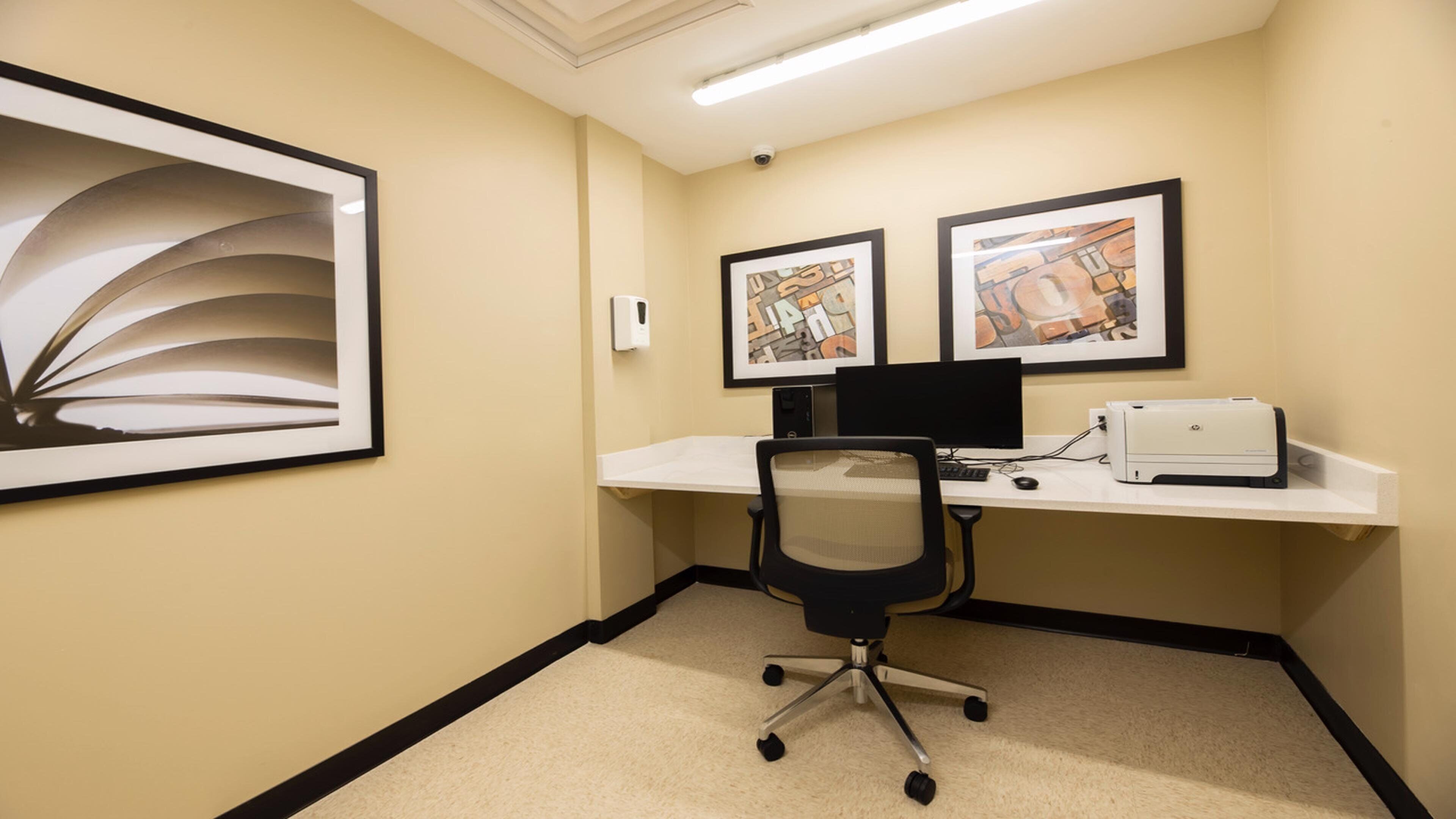 A small office space with a desk, chair, computer, and two framed artworks on the wall.