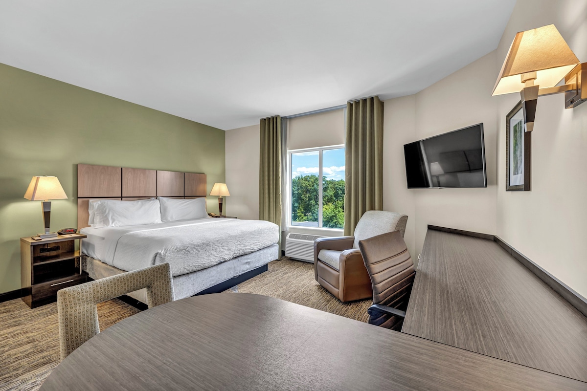Ein Hotelzimmer mit Bett, Schreibtisch, Stuhl, Fernseher und einem Fenster mit Vorhängen.