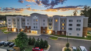 A multi-story hotel with a central entrance, parking lot, and surrounding greenery. - Candlewood Suites Dumfries - Quantico by IHG (Dumfries)