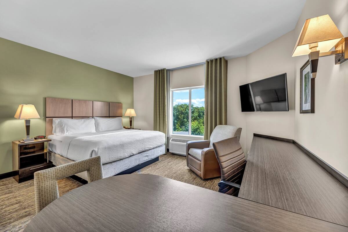 Una habitación de hotel con cama, escritorio, silla, televisor y ventana con cortinas.