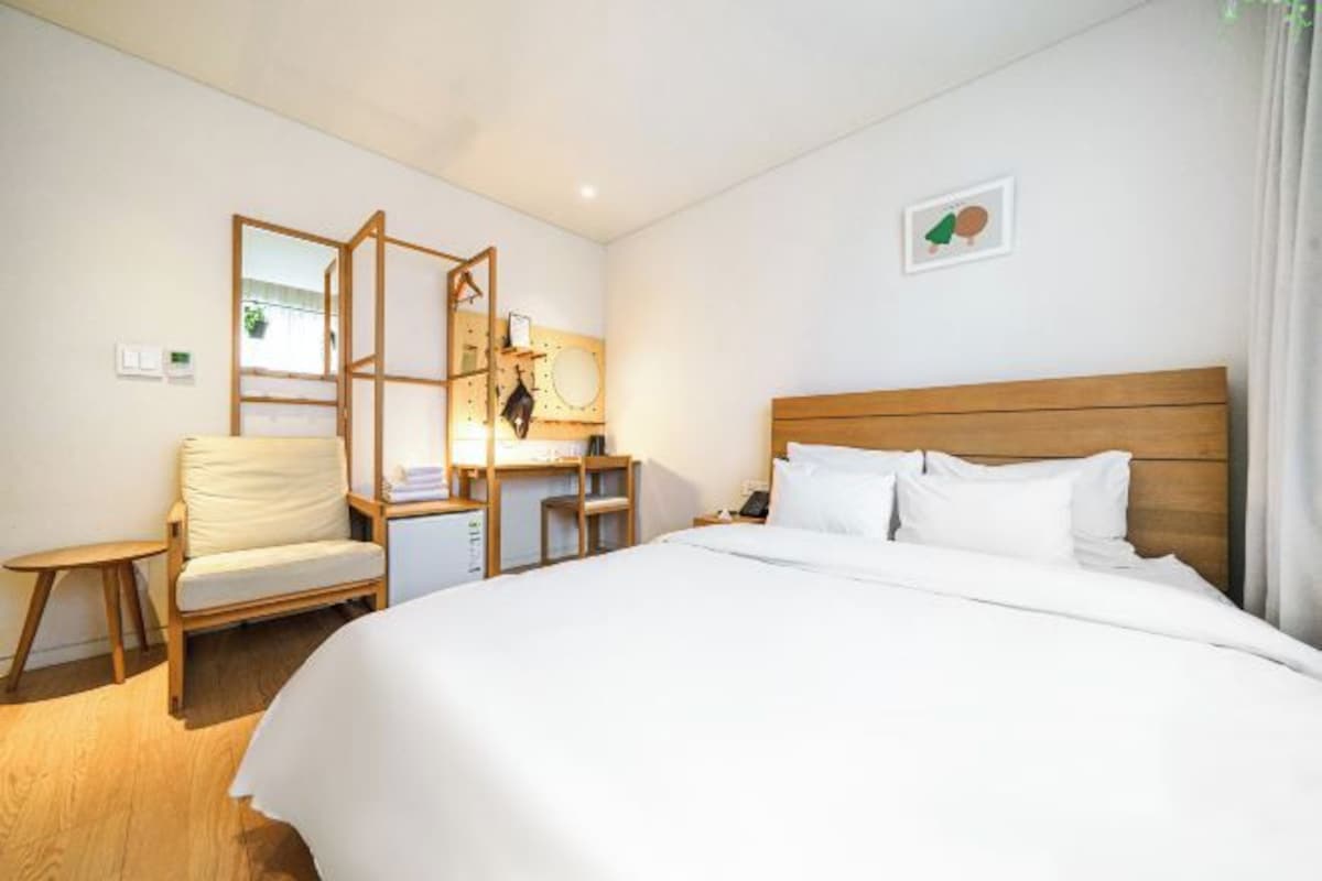 Une chambre d’hôtel avec un grand lit, une tête de lit en bois, un bureau avec une chaise et une petite table.
