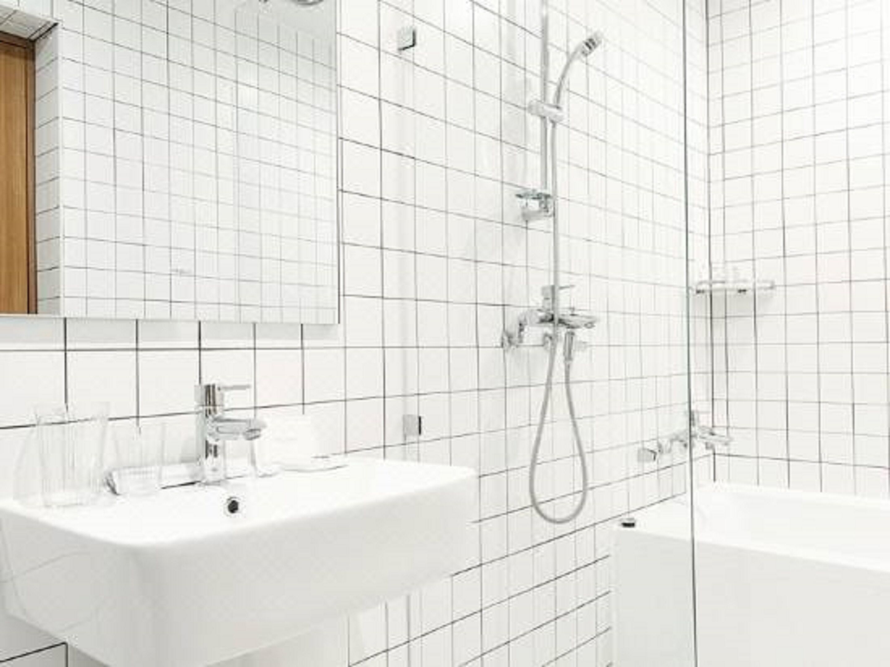 A modern bathroom with white tiles, a sink, a bathtub, and a shower.