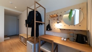 Une petite chambre comprenant un lit superposé, un bureau avec un miroir, une machine à café et une plante suspendue.