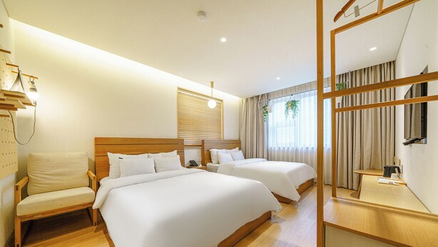 A hotel room with two beds, a wooden chair, a desk, and a mirror. - Chuncheon Hey Hotel (Chuncheon)