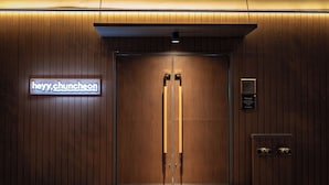 Une entrée avec une double porte en bois, surmontée d’un panneau néon indiquant « hey y chuncheon » et d’une plaque portant une inscription.