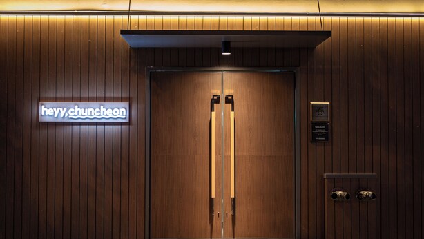 A wooden double door entrance with a neon sign reading "hey y chuncheon" and a plaque with text. - Chuncheon Hey Hotel (Chuncheon)