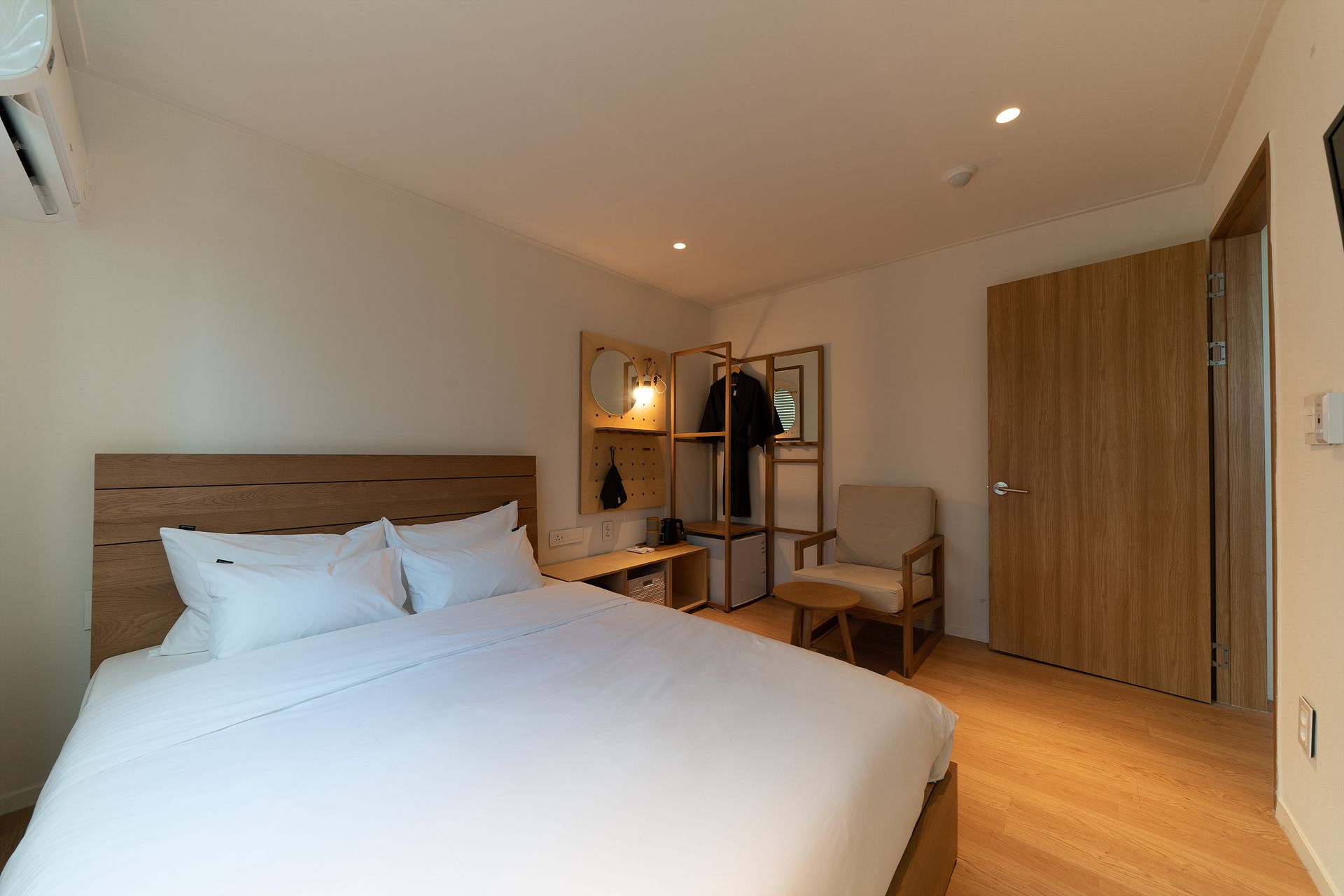 A hotel room with a large bed, a desk with a chair, a wardrobe, and a mirror.