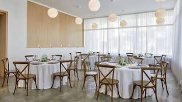A spacious room with multiple round tables set for dining, wooden chairs, and pendant lighting.