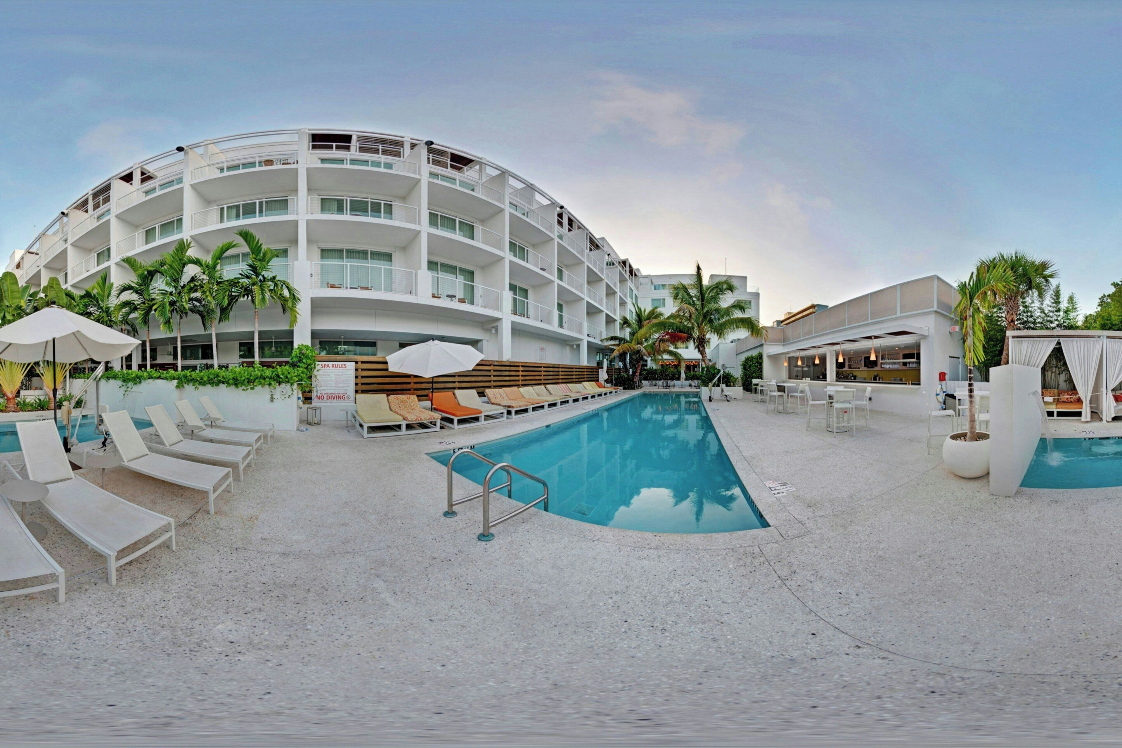 Un hotel moderno con una piscina grande, tumbonas y palmeras.