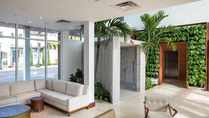 A modern hotel lobby with a sectional sofa, a round coffee table, and a chair. There is a concrete pillar and a wall with green plants. - The Sarasota Modern, a Tribute Portfolio Hotel (Sarasota)