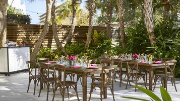 Un área de comedor al aire libre con mesas y sillas de madera, rodeada de exuberante vegetación y palmeras.