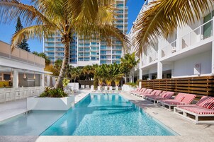 A swimming pool with lounge chairs, palm trees, and a high-rise building in the background.