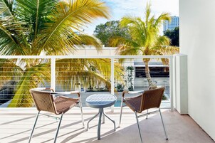 A balcony with two wicker chairs and a small round table, overlooking a pool and palm trees.