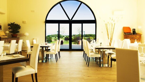 A dining area with tables and chairs, a large arched window, and a view of greenery outside. - Tenuta Lamborghini Golf & Resort (Panicale)