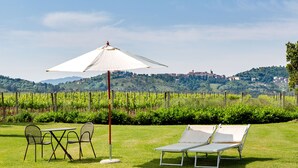 A grassy outdoor area with a table and chairs, a sun umbrella, and two lounge chairs. - Tenuta Lamborghini Golf & Resort (Panicale)