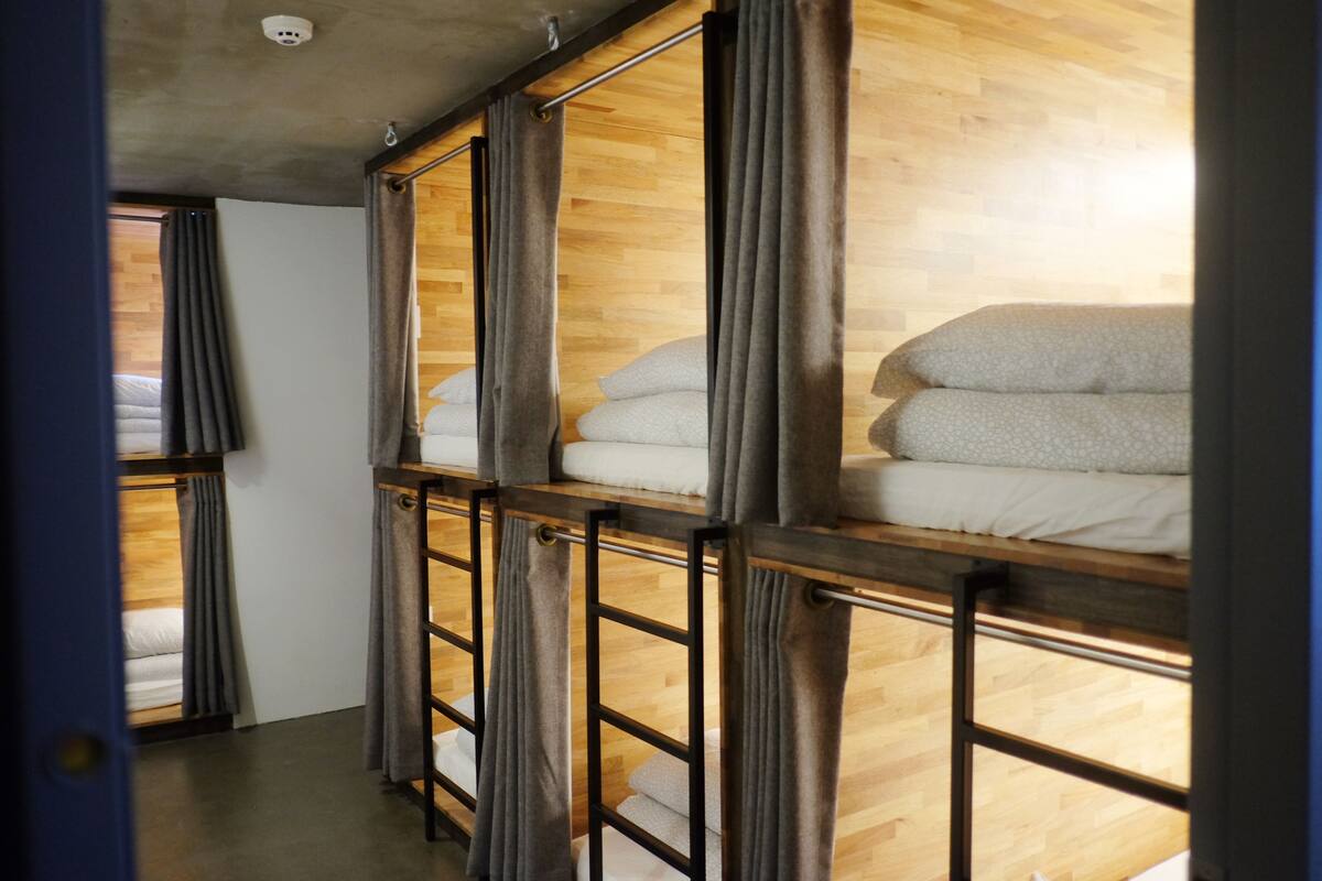 A room with bunk beds, wooden flooring, and curtains.