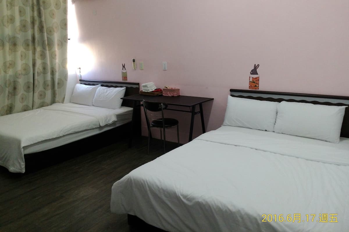 A hotel room with two single beds, a desk, a chair, and a small table.