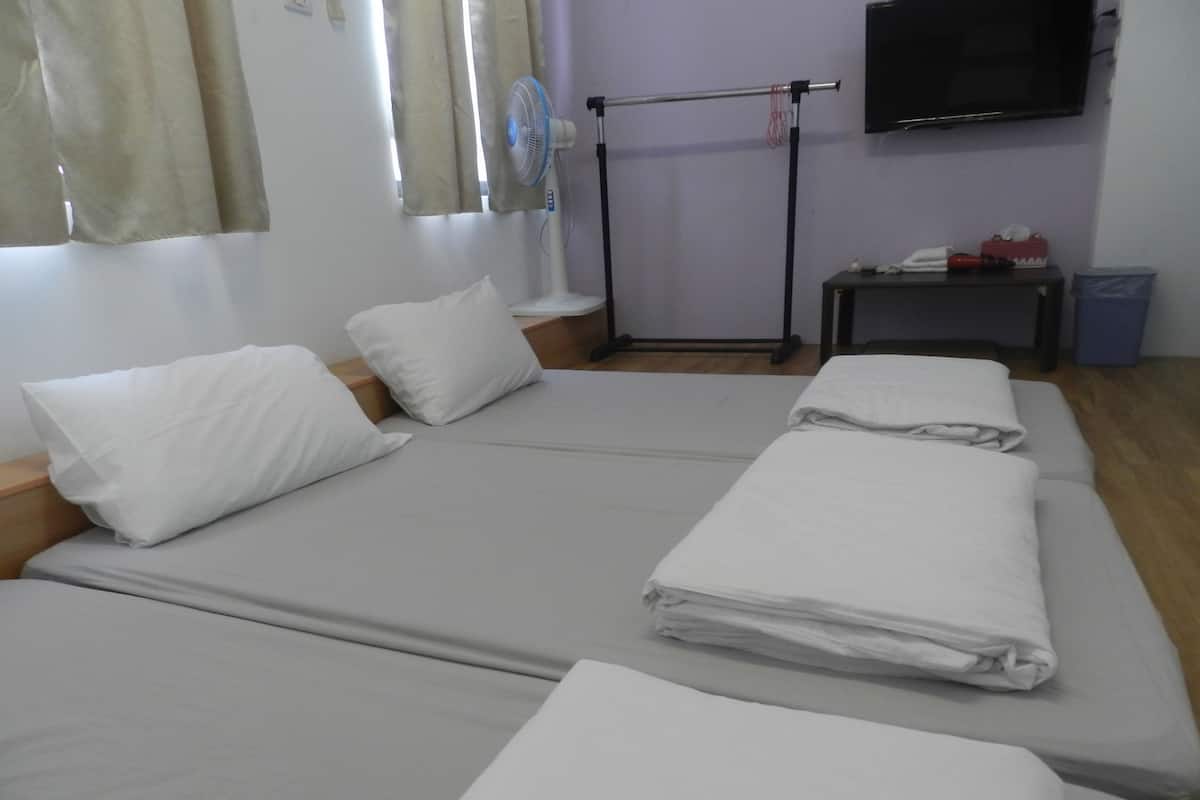 A hotel room with two beds, a TV mounted on the wall, a fan, and a small table with a trash bin.