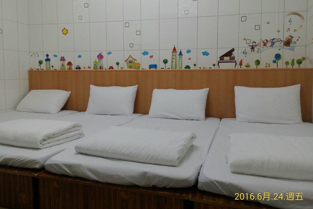 A hotel room with three beds, white linens, and a colorful wall mural.