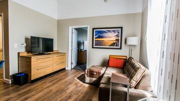 A modern living room with a flat-screen TV, wooden furniture, a sofa with cushions, and a framed picture on the wall.