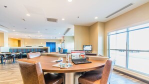 A modern hotel lobby with a round table, leather chairs, a laptop, and a large window offering a view of the street. - Towneplace Suites by Marriott Evansville Newburgh (Newburgh)