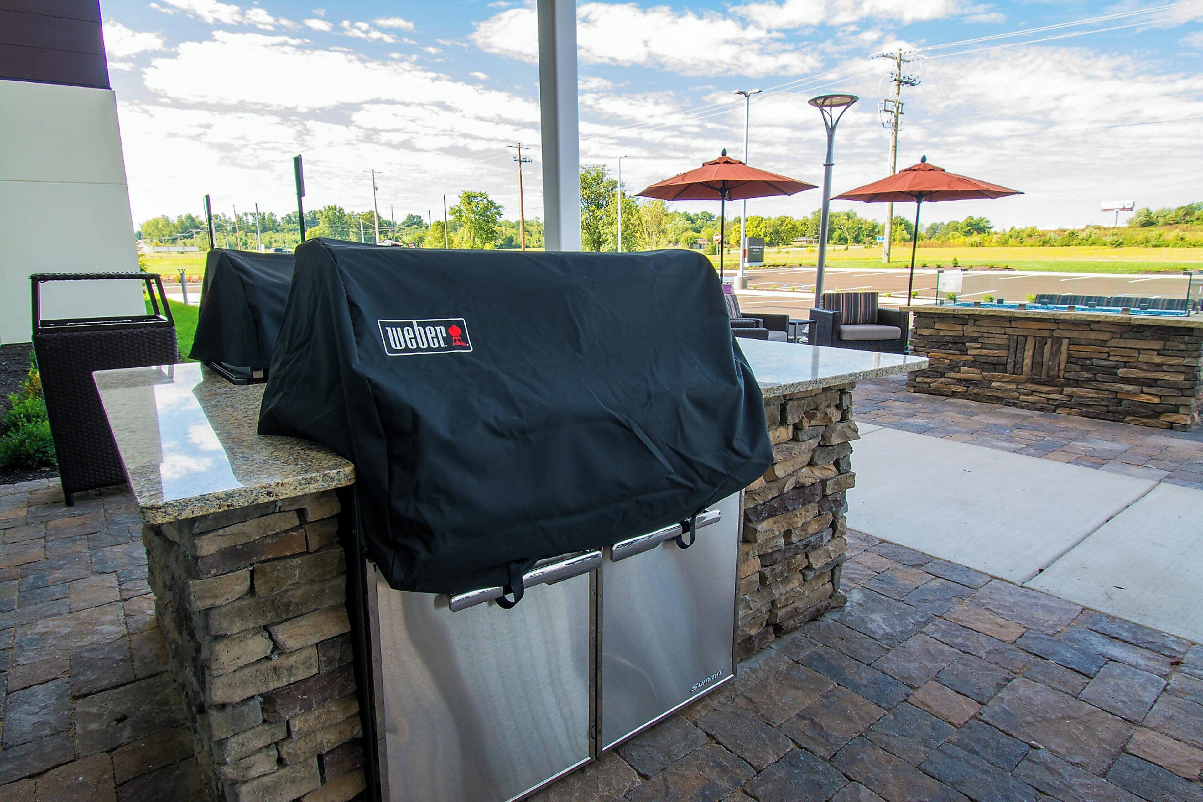 An outdoor bar area with a stone counter, grill covers, and outdoor seating with umbrellas.