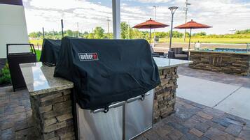 An outdoor bar area with a stone counter, grill covers, and outdoor seating with umbrellas.