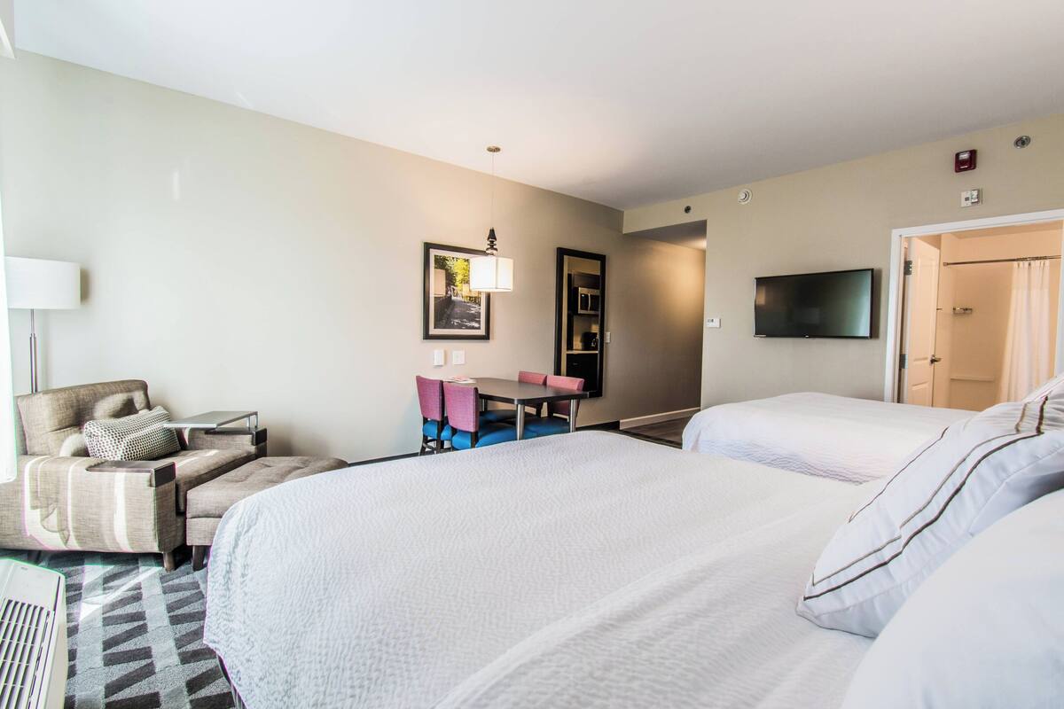 Hotellihuone, jossa on kaksi sänkyä, työpöytä, tuoli, televisio ja ovi, joka johtaa kylpyhuoneeseen.