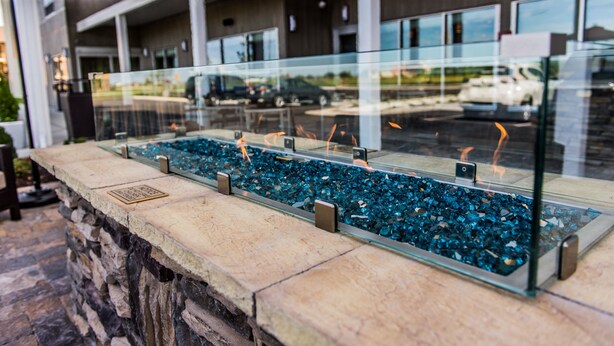 A glass-top fire feature with blue glass pebbles, set in a stone structure. - Towneplace Suites by Marriott Evansville Newburgh (Newburgh)