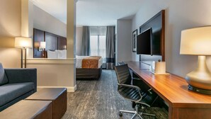 Habitación de hotel con cama, escritorio, silla, sofá, televisor y lámpara.