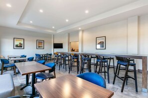 Un espace repas moderne avec des tables en bois et des chaises bleues, un coin bar avec des tabourets et des tableaux encadrés aux murs.
