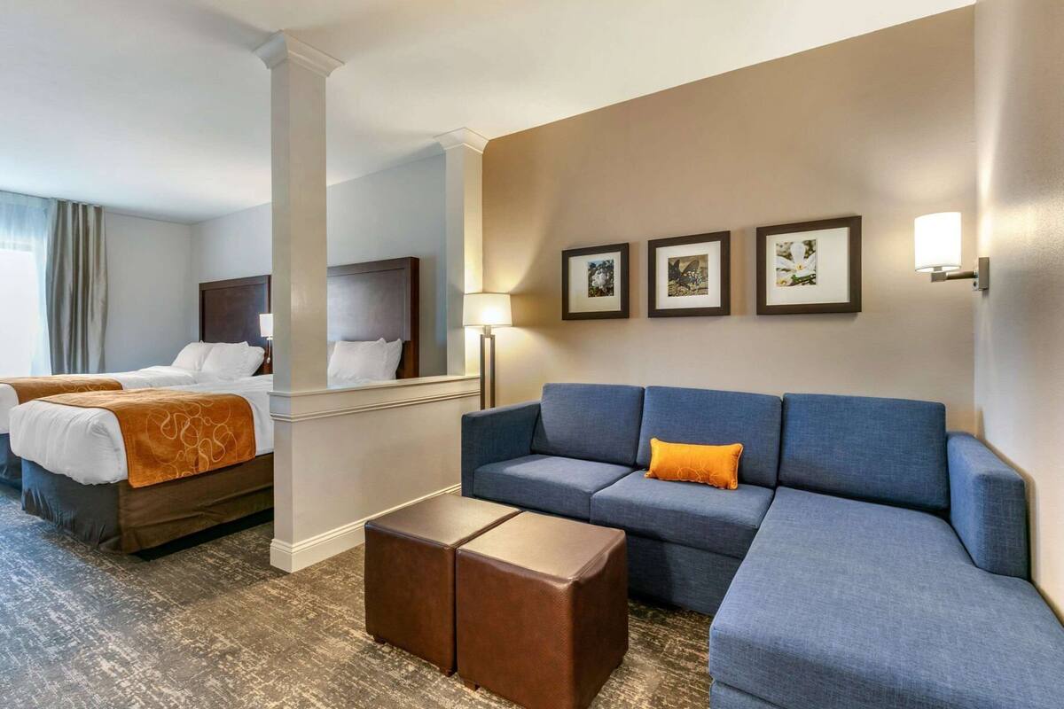 A hotel room with two beds, a sofa, a coffee table, and framed pictures on the wall.