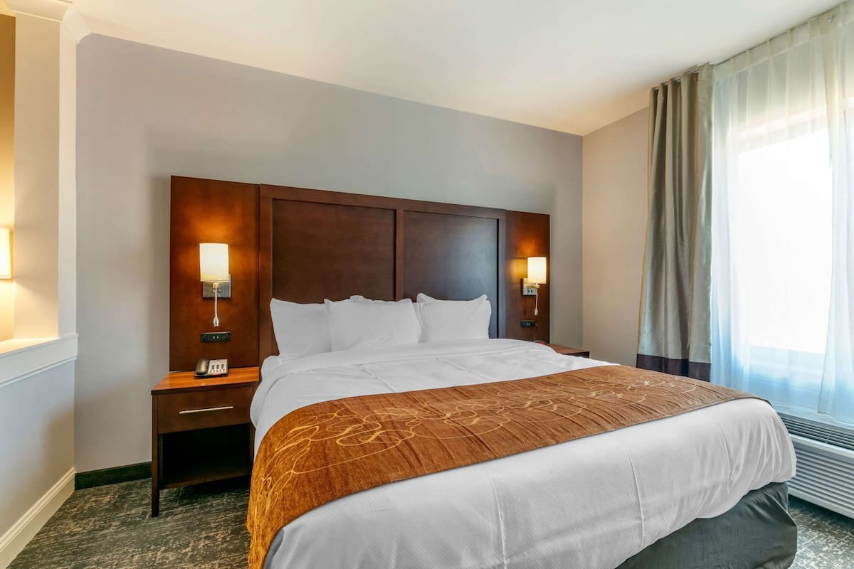A hotel room with a large bed, two bedside tables with lamps, a telephone, and a window with curtains.
