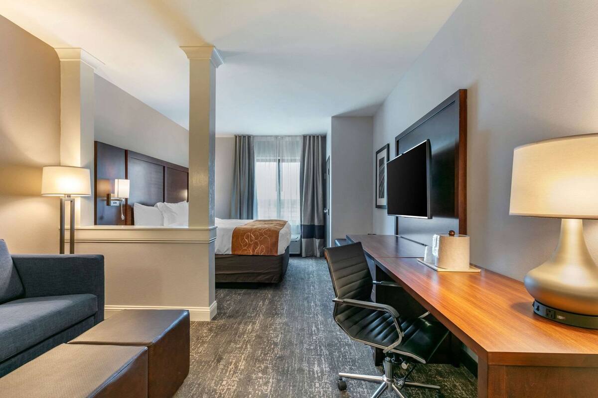 A hotel room with a bed, a desk with a chair, a television, and a sofa.