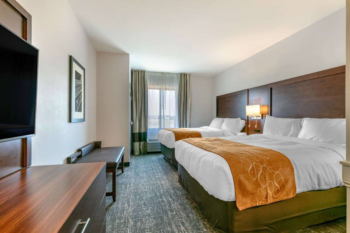 A hotel room with two beds, a desk, a TV, and a window with curtains.