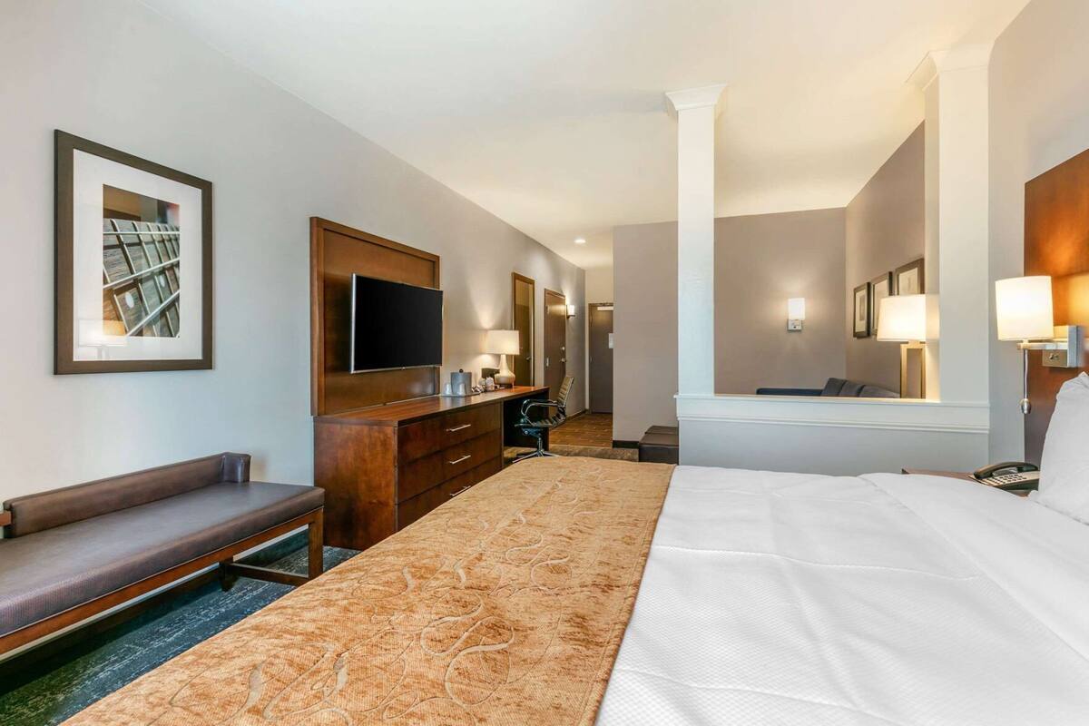 A hotel room with a bed, a desk, a chair, a television, and a mirror.
