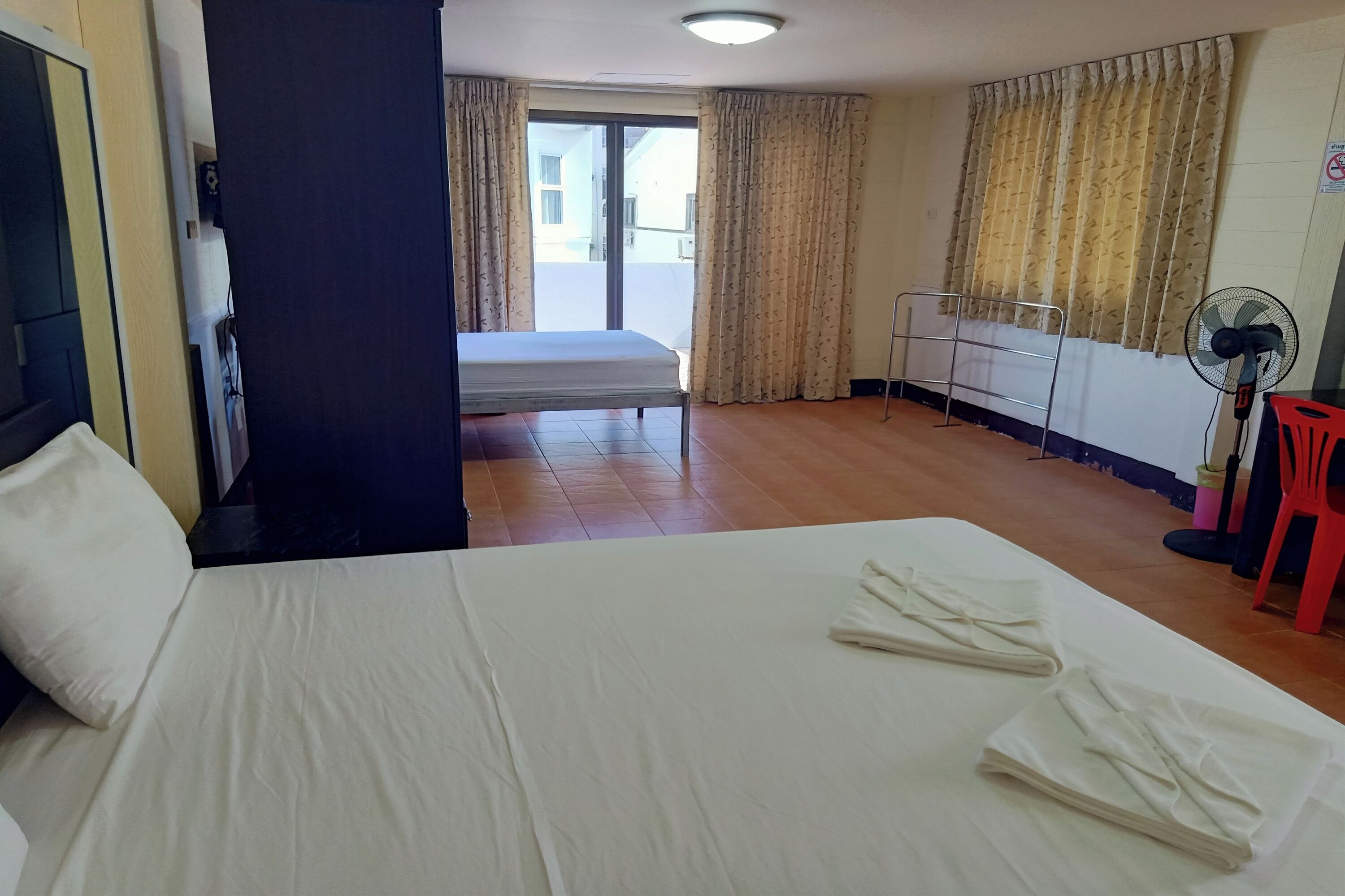 A hotel room with a bed, a window with curtains, a radiator, and a standing fan.