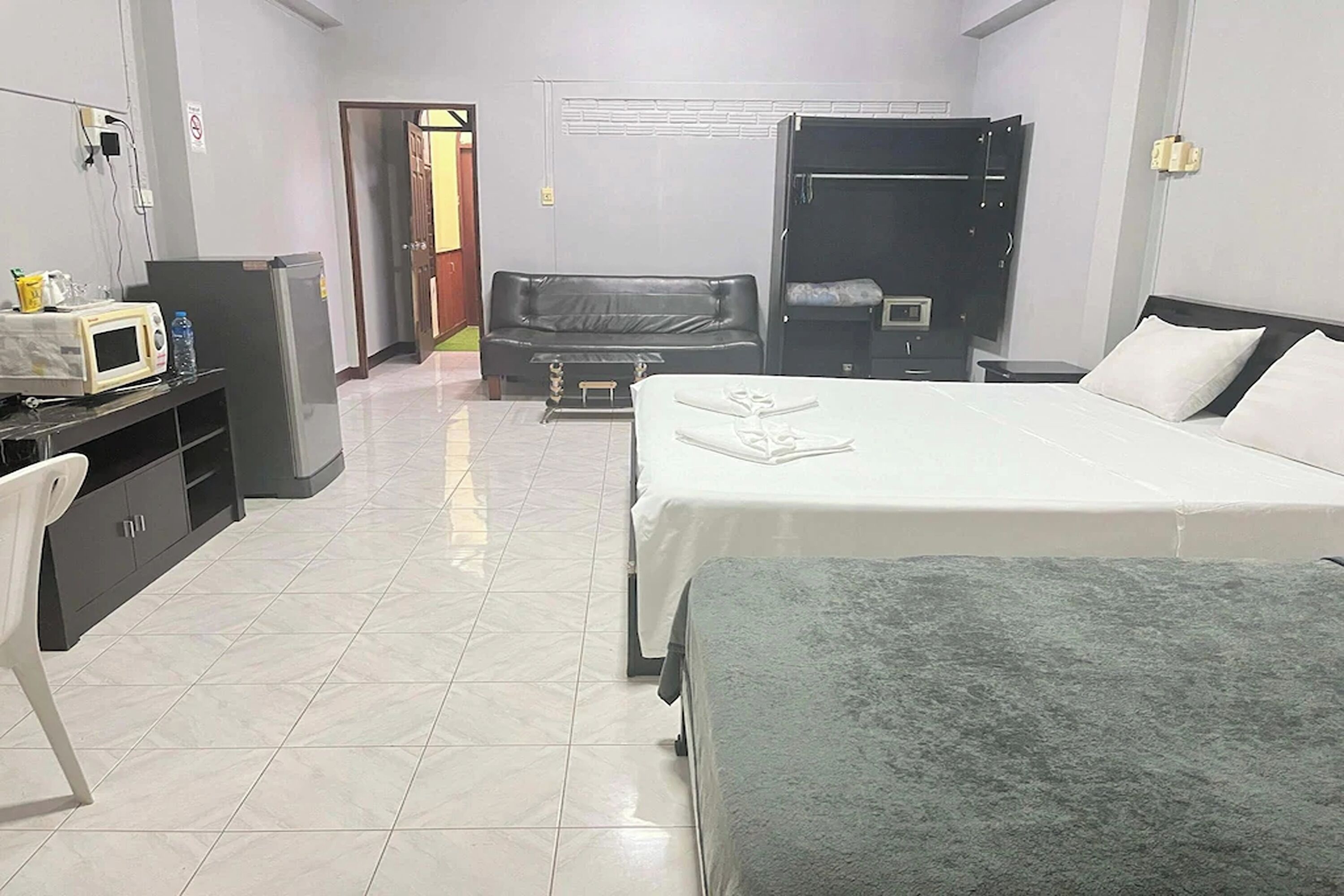 A hotel room with a bed, a desk with a microwave, a wardrobe, and a sofa.