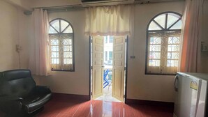 Quarto com piso de ladrilho vermelho, uma poltrona de couro preto, uma geladeira branca e uma porta que dá para área externa.