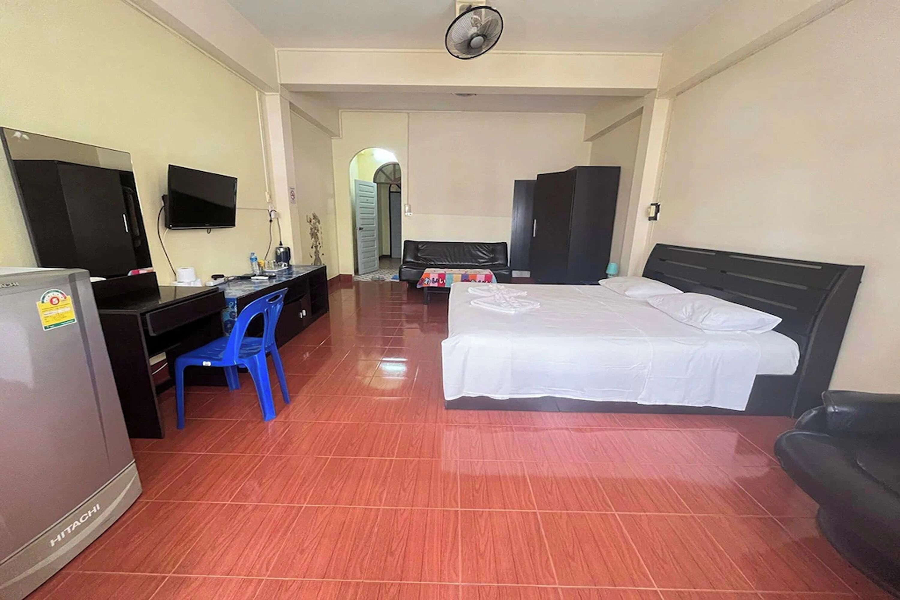 A hotel room with a bed, a desk with a chair, a television, and a refrigerator.