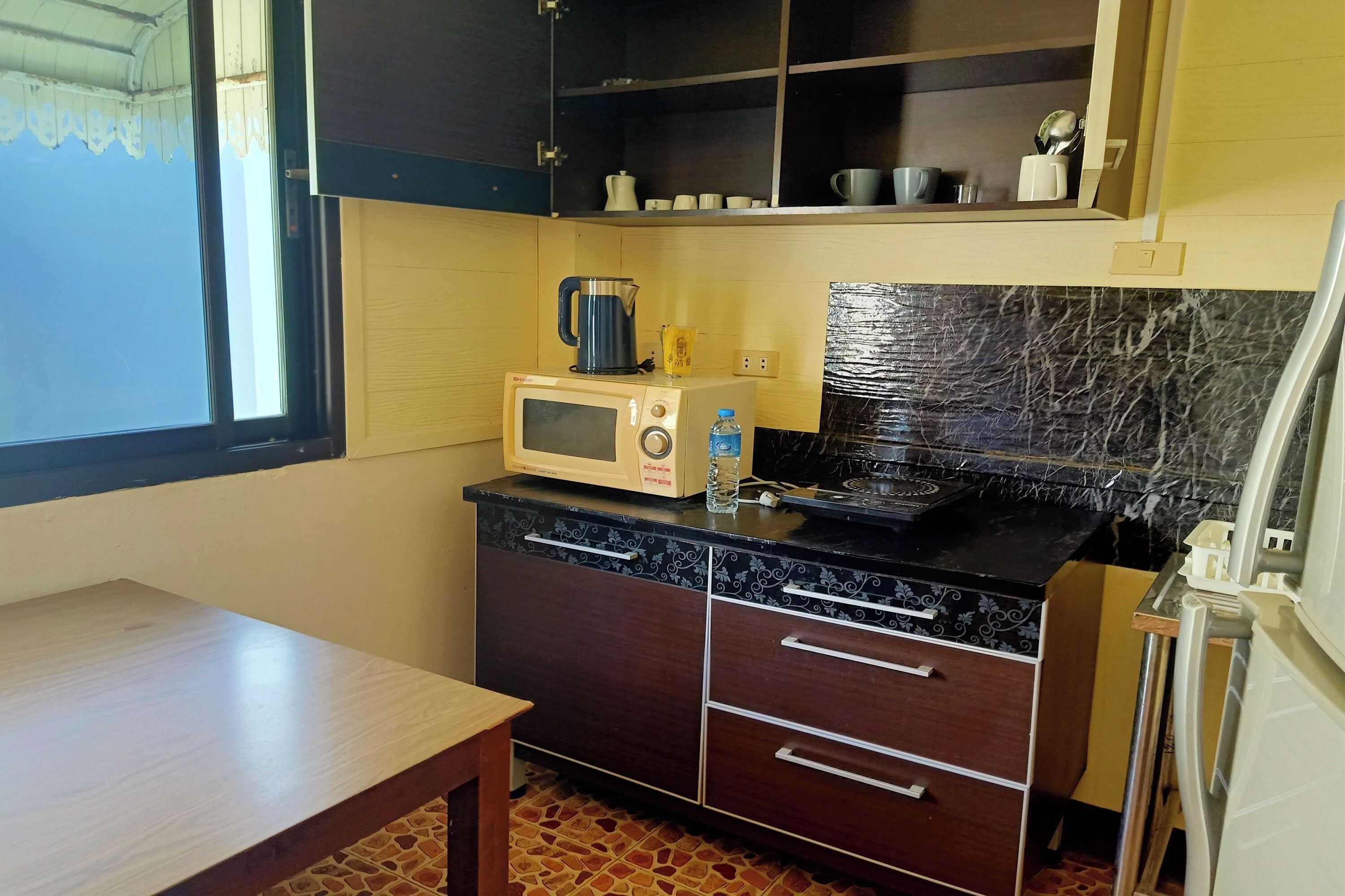 A compact kitchen with a microwave, kettle, and water bottle on the counter, a small table, and cabinets with drawers.