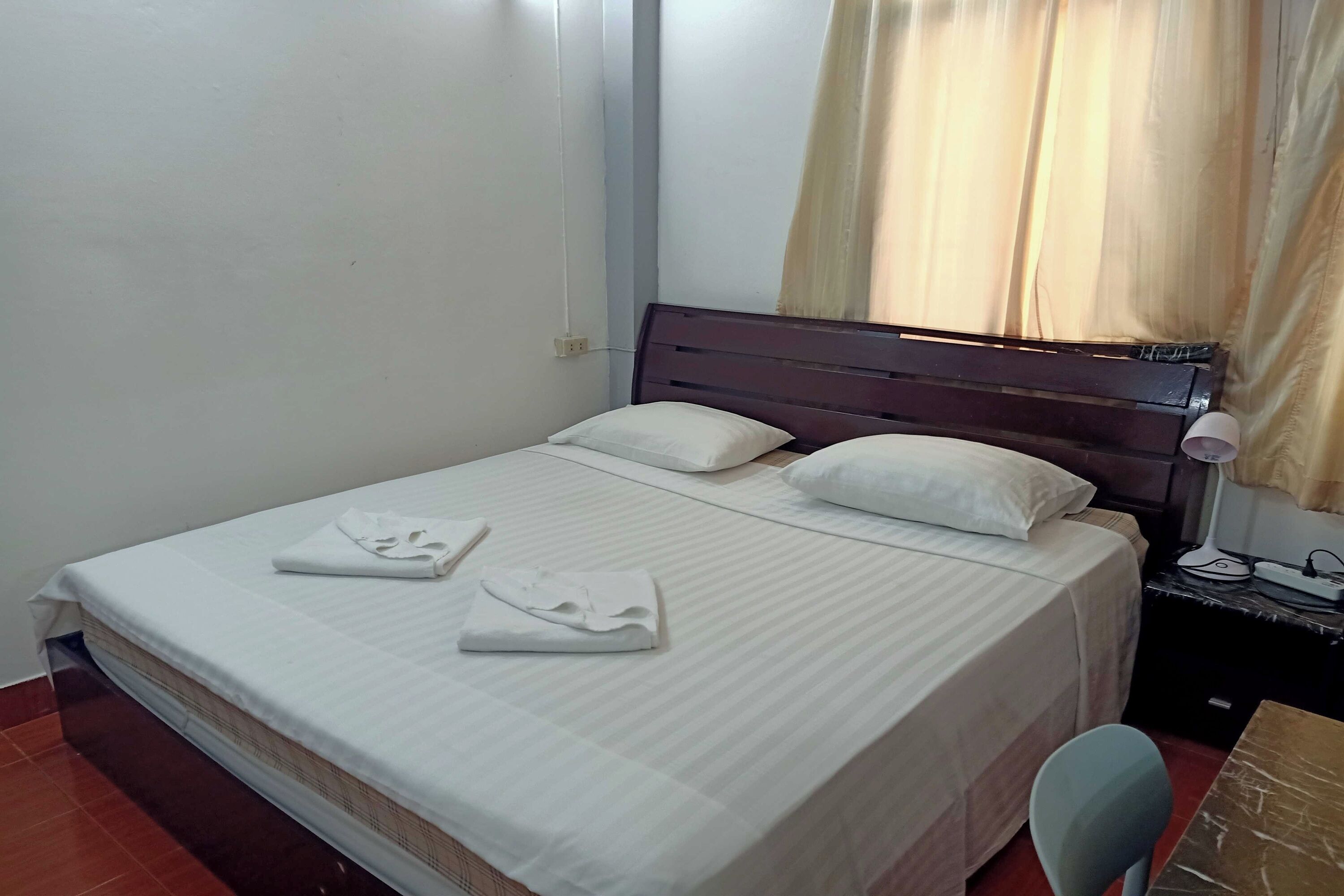 A neatly made bed with pillows and folded towels, a bedside table with a lamp, and a chair.