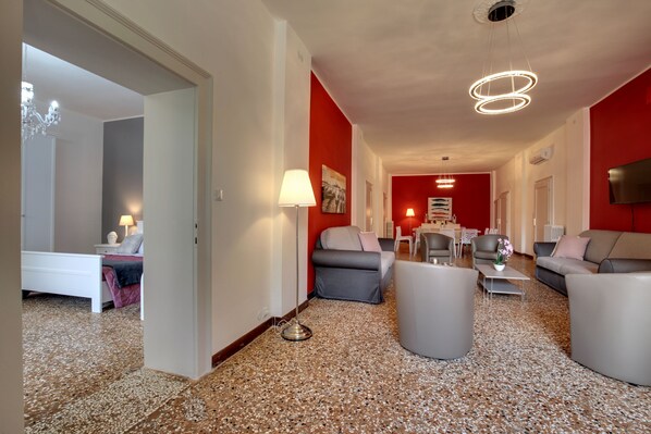 A modern living room with a red accent wall, a chandelier, and a flat-screen TV. - Accademia Opera Deluxe by Wonderful Italy (Venice)