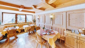 Un espace repas avec des tables et des chaises en bois, un buffet et une vue sur l’extérieur grâce à de grandes fenêtres.