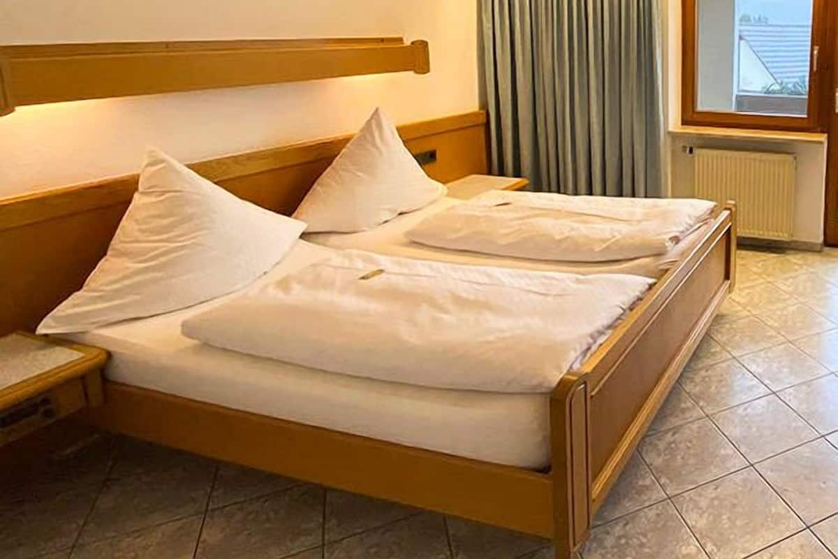 A hotel room with a double bed, wooden headboard, a window with curtains, and a radiator.